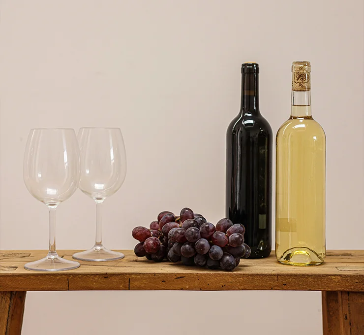 A bottle of white wine and a bottle of Spanish red wine, alongside a bunch of grapes, on a wooden table